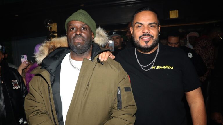Funk Flex wearing a green beanie and parka jacket standing next to DJ Enuff in a black “The Heavy Hitters” t-shirt at a hip-hop event.