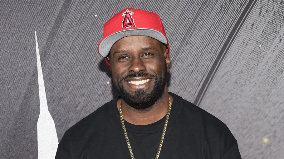 Funk Flex wearing a red Los Angeles Angels cap and black shirt, smiling on the red carpet.