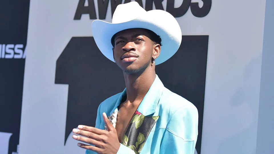 Lil Nas X wearing a white cowboy hat and turquoise jacket on the BET Awards red carpet.