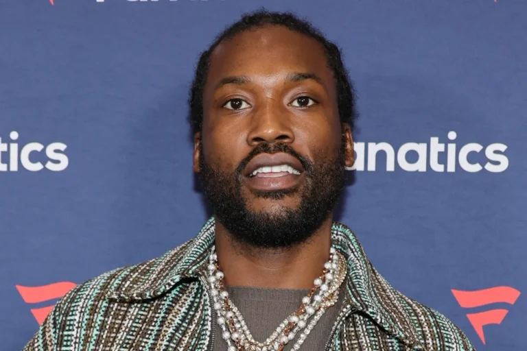 Meek Mill wearing a patterned jacket with layered pearl necklaces while posing on the red carpet at the Fanatics event.