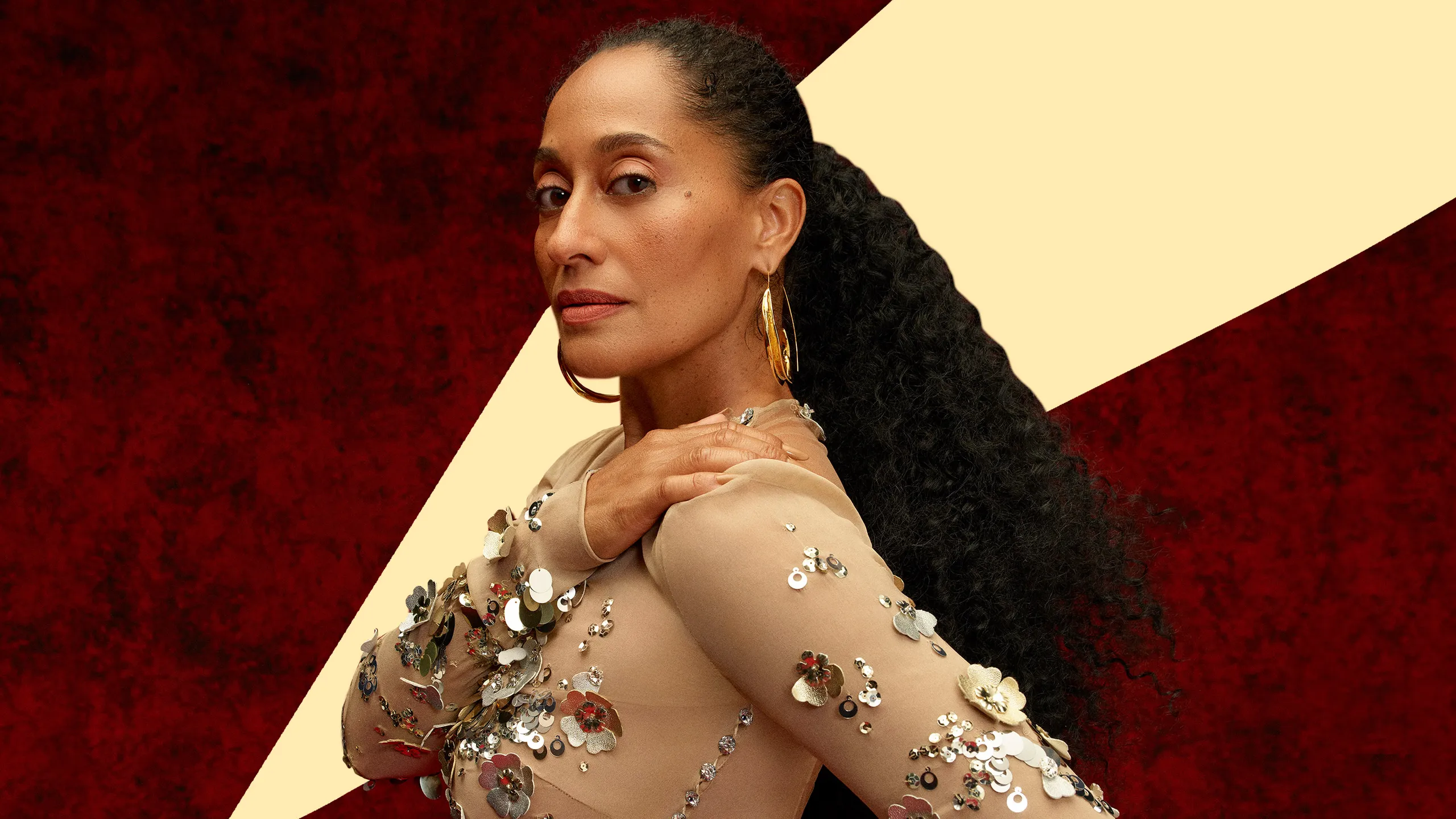 Tracee Ellis Ross wearing a nude gown with sequined floral embellishments, large gold hoop earrings, and her hair styled in a sleek ponytail.