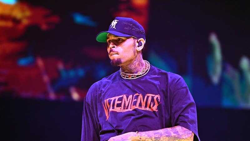 Chris Brown performing live on stage in 2025 wearing a black Vetements shirt and a baseball cap.