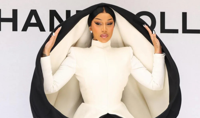 Cardi B wearing a white structured jacket framed by a large black circular sculptural piece at Paris Fashion Week.