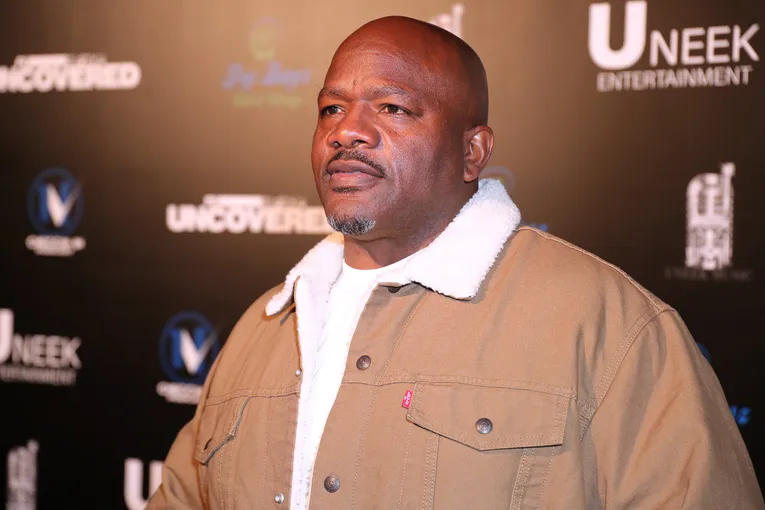 Eugene Big U Henley standing on the red carpet at a UNEEK Entertainment event wearing a brown jacket with white fleece collar.