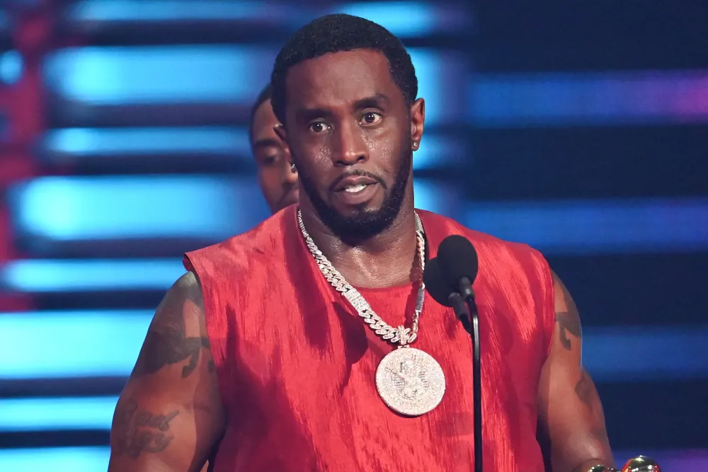 Diddy wearing a red sleeveless outfit and diamond chain speaking on stage during an award show.