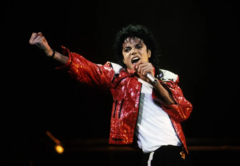 Michael Jackson wearing a red sequined jacket and performing passionately on stage with a microphone in hand.