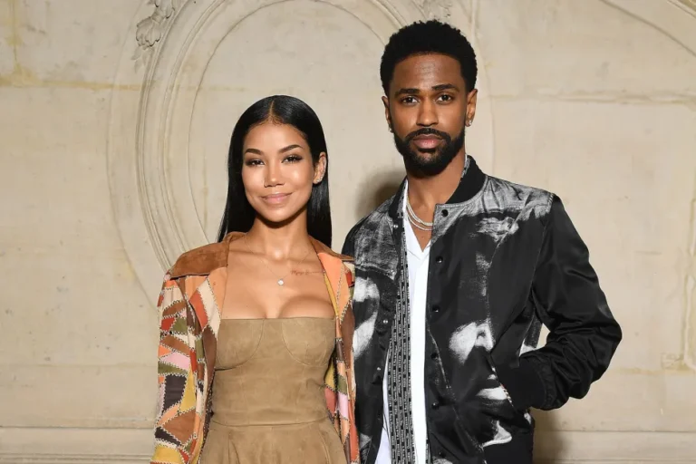 Big Sean and Jhené Aiko smiling together at an event, dressed in coordinated casual outfits.