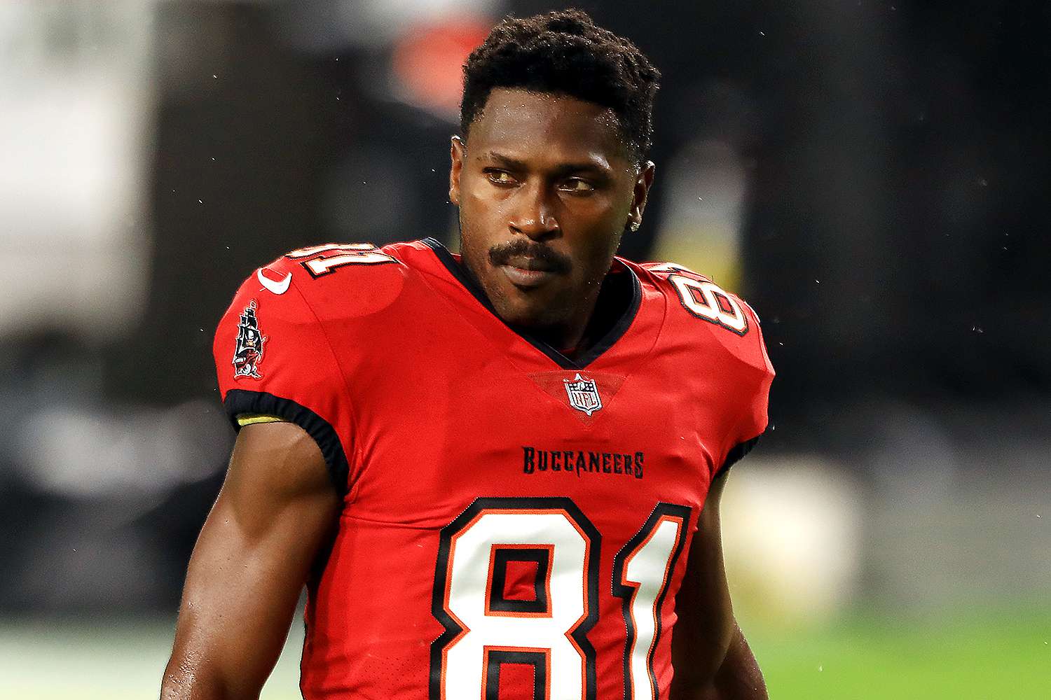 Antonio Brown in a red Tampa Bay Buccaneers jersey with number 81, standing on the football field during a night game.