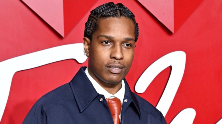 A$AP Rocky wearing a navy jacket and red tie while attending a red carpet fashion event.